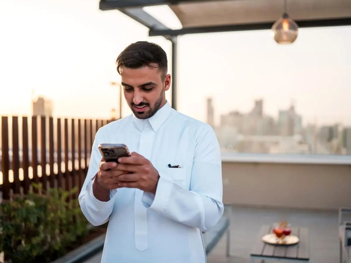 شاب يستخدم تطبيق iSpeaker على هاتفه في سطح منزل وقت الغروب